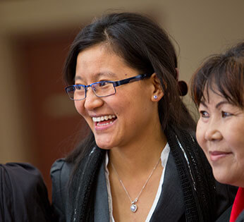 A female international student is smiling with her arm around the shoulder of an older woman